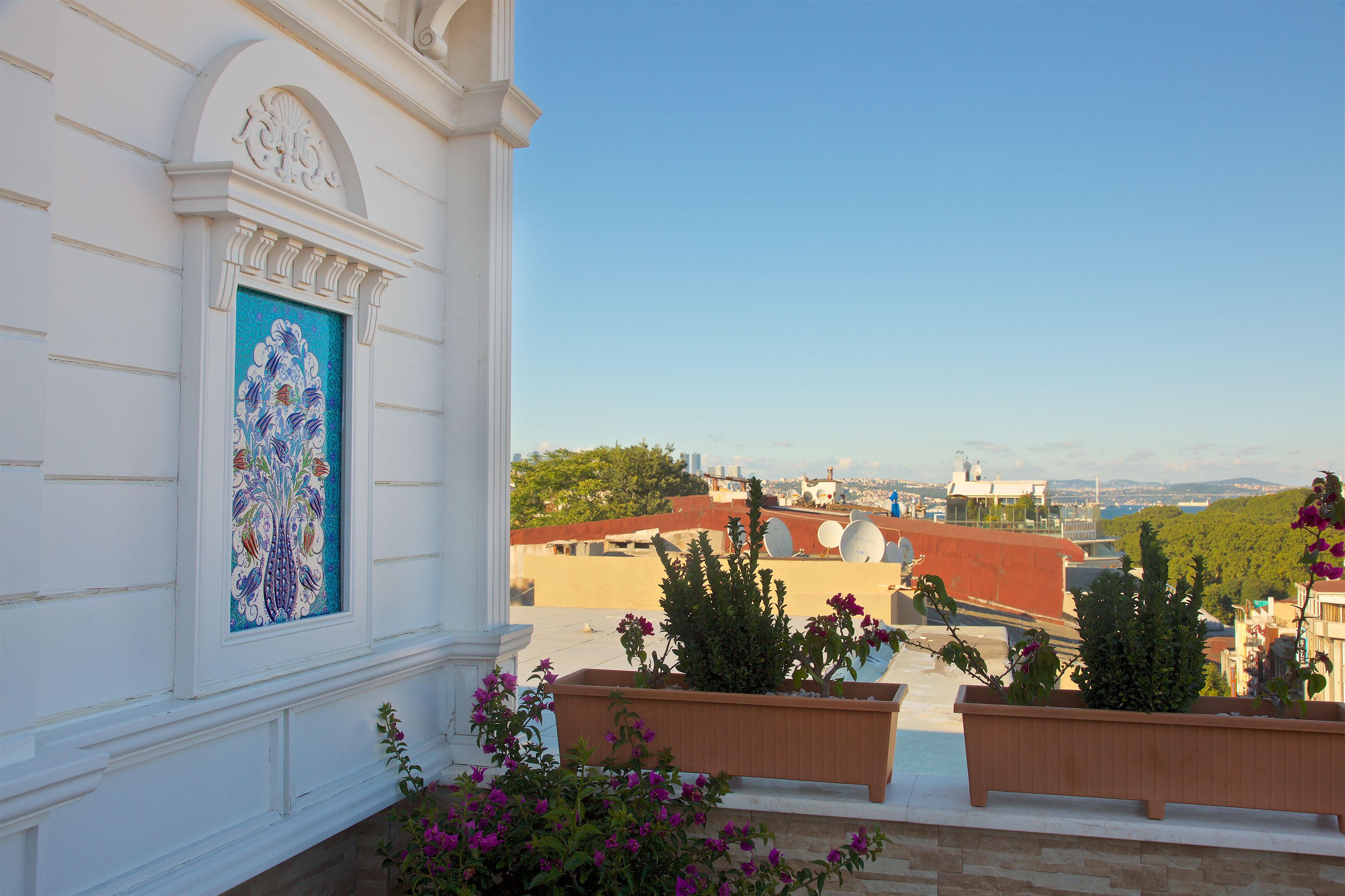 A balcony with a view of a cityscape, a decorative window, and potted plants.