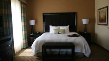 A hotel room with a large bed, two bedside tables with lamps, a bench, a dresser, and a painting on the wall.