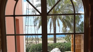Vista a través de una ventana con un diseño de cuadrícula, que da a un espacio al aire libre con palmeras, una torre de construcción y un sendero pavimentado.