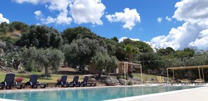 A pool area with lounge chairs, a pergola, and a view of trees and rocks. - Relais Casa Mirabile (Menfi)