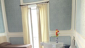 A living room with a sofa, a small table with cups, a chair, and a window with curtains. - Dimora Annulina B&B (Palermo)
