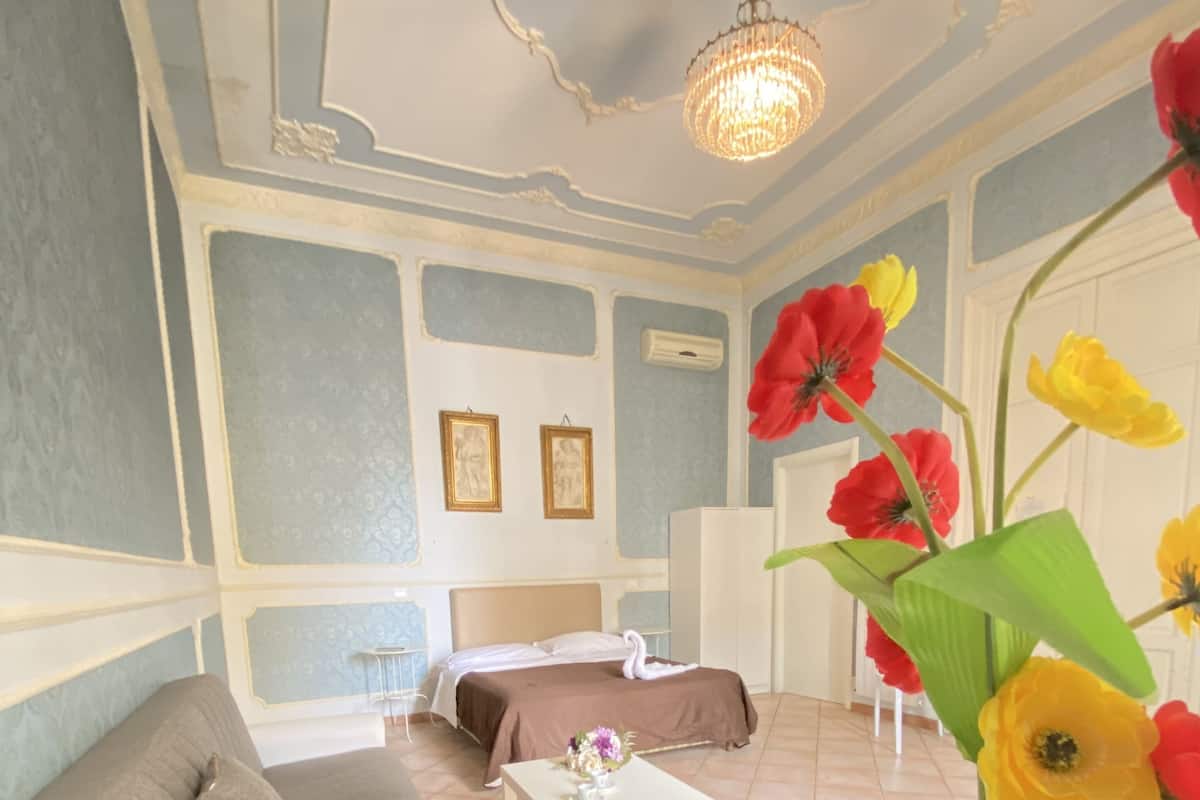 A room with a bed, a sofa, a small table, and a vase with flowers.
