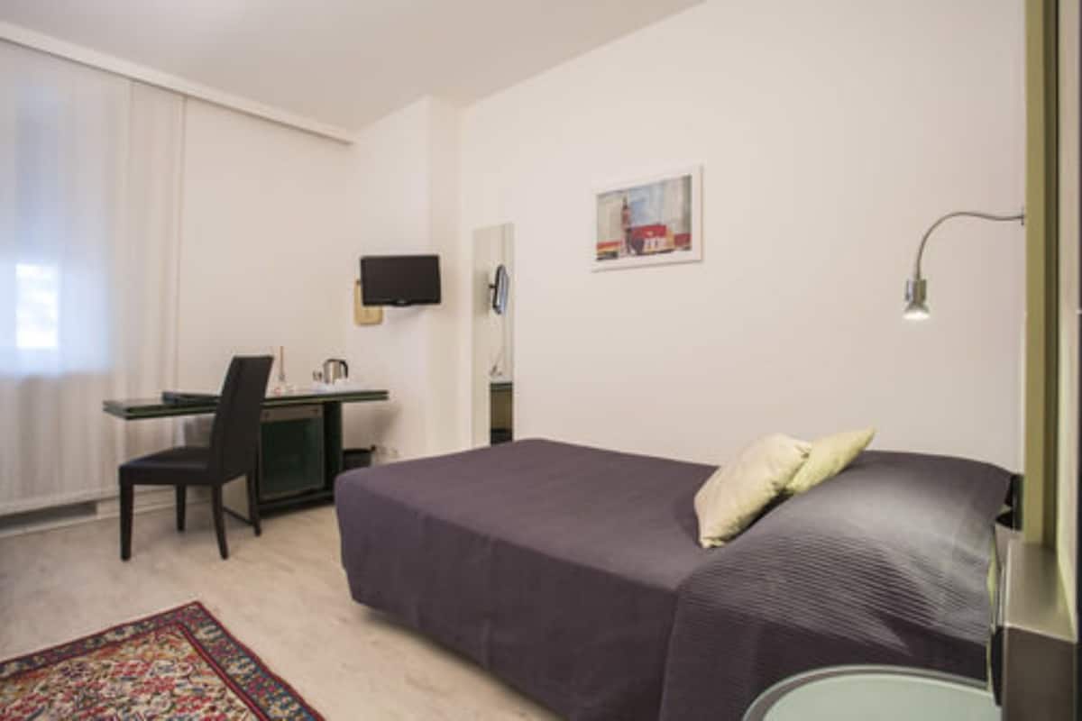 Ein Schlafzimmer mit einem Bett, einem Schreibtisch, einem Sessel, einem Fernseher und einer Lampe.