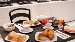 A breakfast table with croissants, pastries, a glass of juice, and a bowl of cereal.