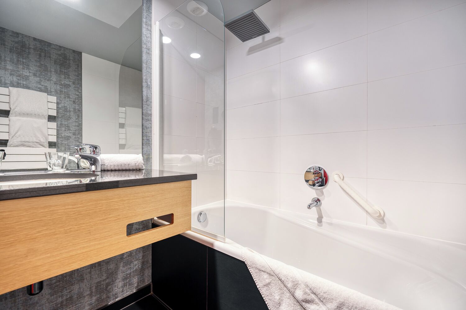 A modern bathroom with a glass shower enclosure, a wooden vanity with a mirror, and a white bathtub.