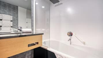 Un baño moderno con cabina de ducha de vidrio, tocador de madera con espejo y bañera blanca.