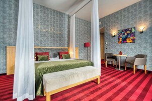 Un dormitorio con una cama con dosel, un banco, un escritorio y sillas.