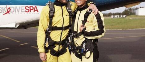 Two people in yellow and black suits standing in front of an airplane with "SKYDIVE SPA" and "00-SEX" written on it.