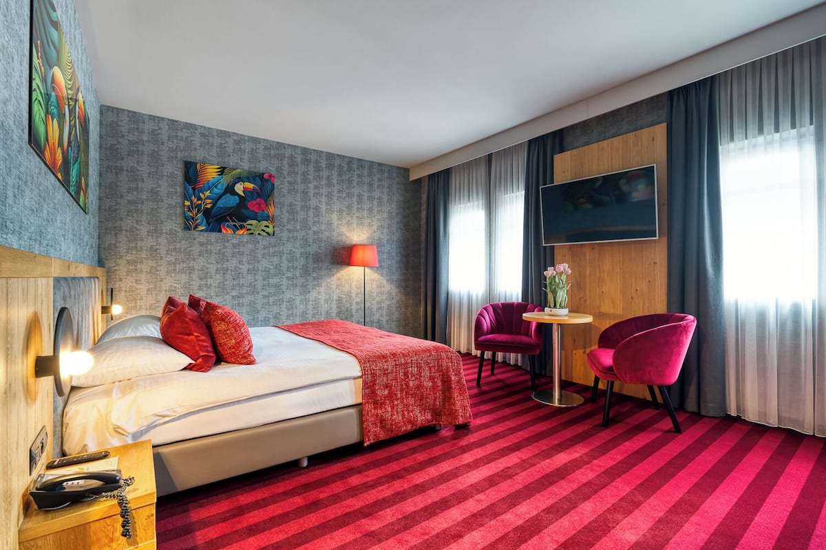 Een hotelkamer met een bed, een bureau, twee stoelen, een lamp en kunst aan de muren.