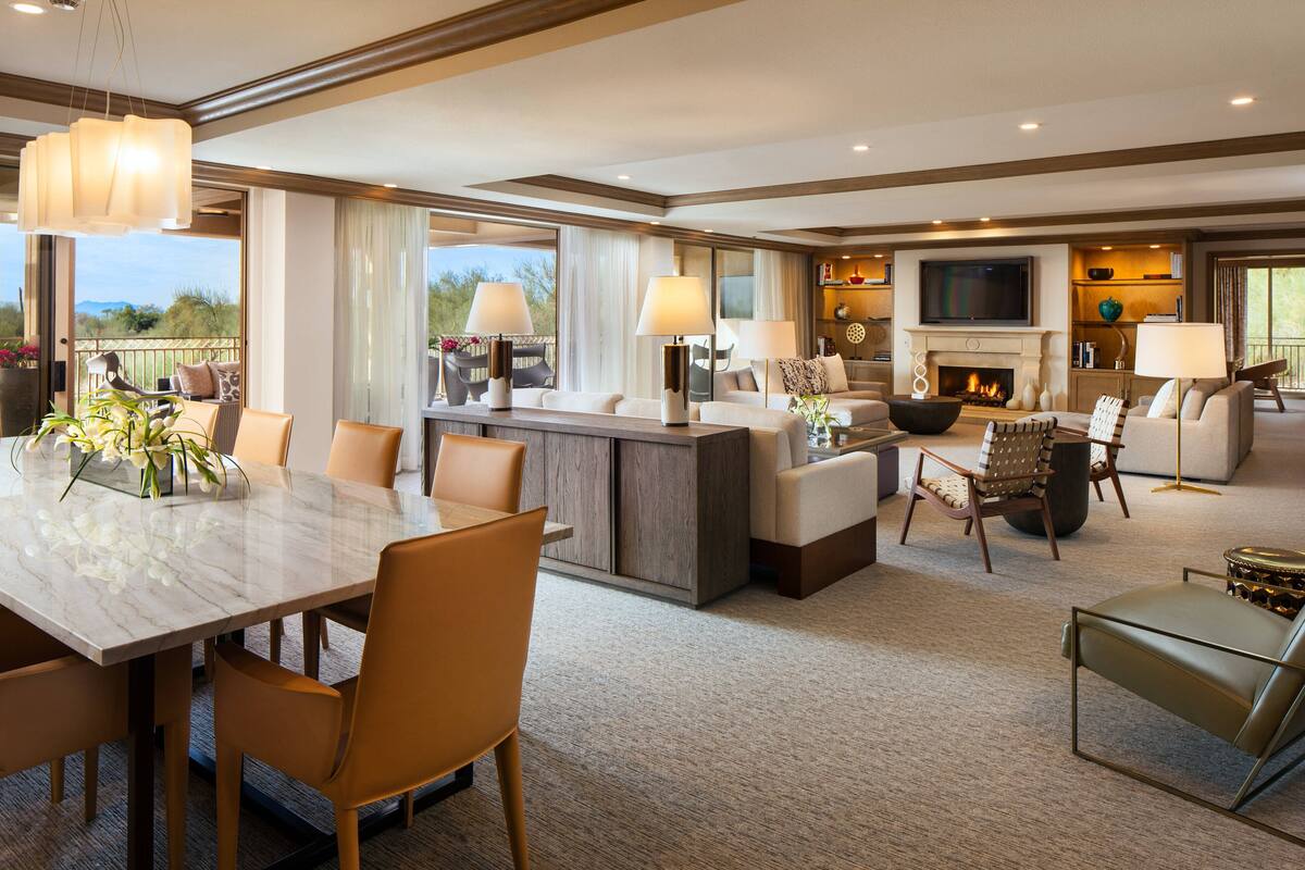 A spacious living area with a marble dining table, comfortable seating, a fireplace, and a television.