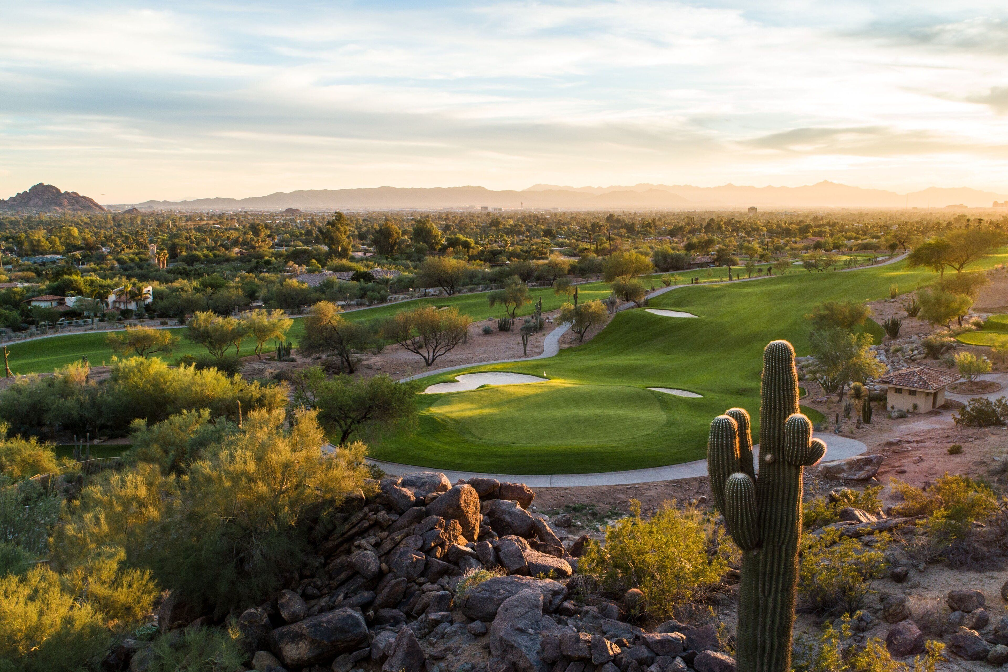 Paisaje desértico con un campo de golf, cactus y montañas a la distancia.