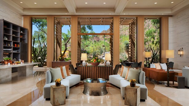 Eine geräumige Lobby mit modernem Design, ausgestattet mit einer zentralen Sitzecke mit Sofas und einem Couchtisch, einer Rezeption und einem großen Fenster mit Blick ins Freie.