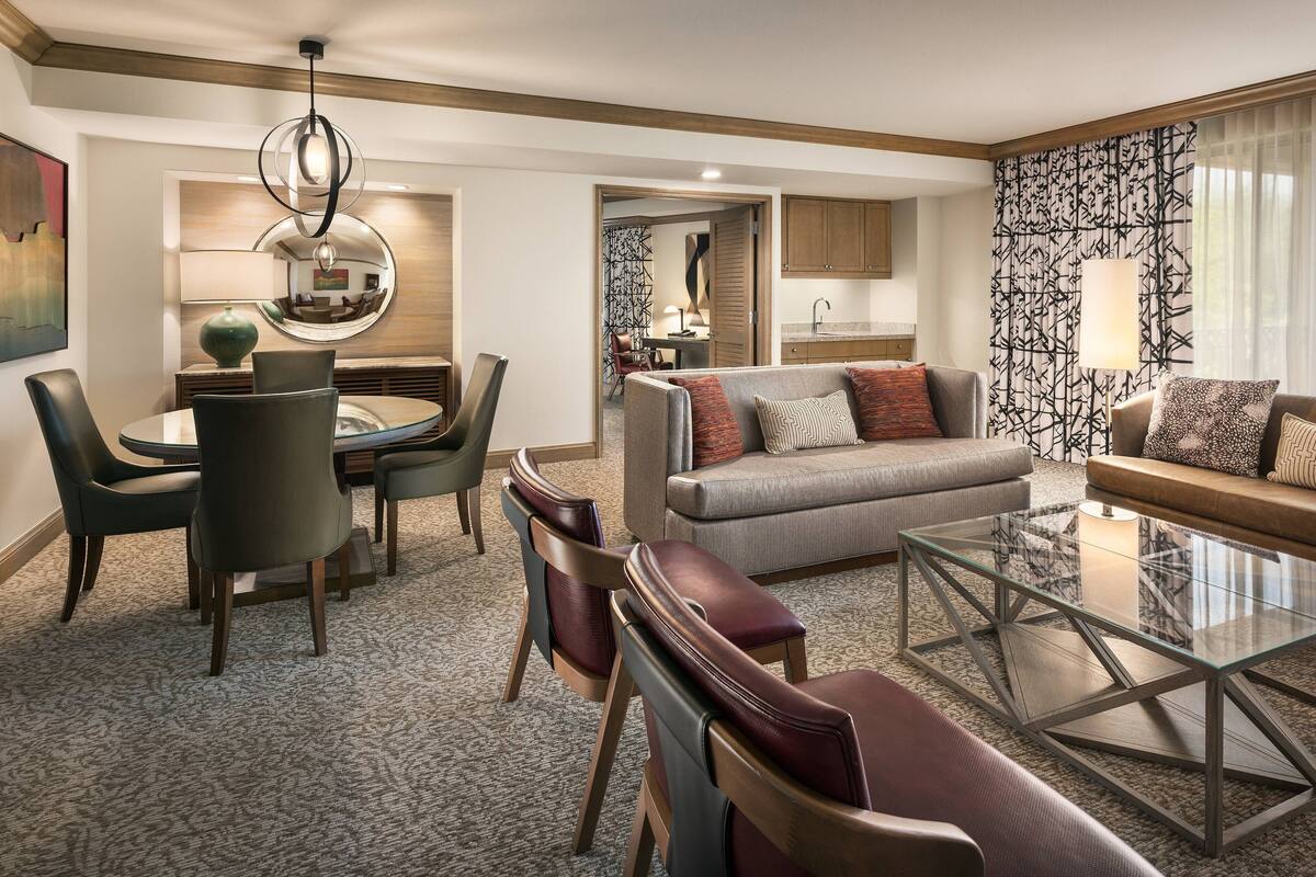 A modern living room with a glass coffee table, leather sofas, and a dining area with a round table and chairs.