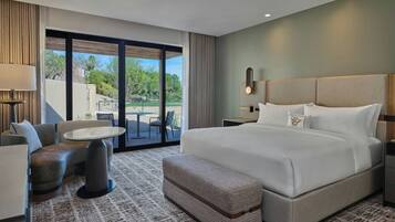 Habitación de hotel con una cama grande, una zona de estar con mesa y vistas a un espacio exterior a través de una puerta de cristal.