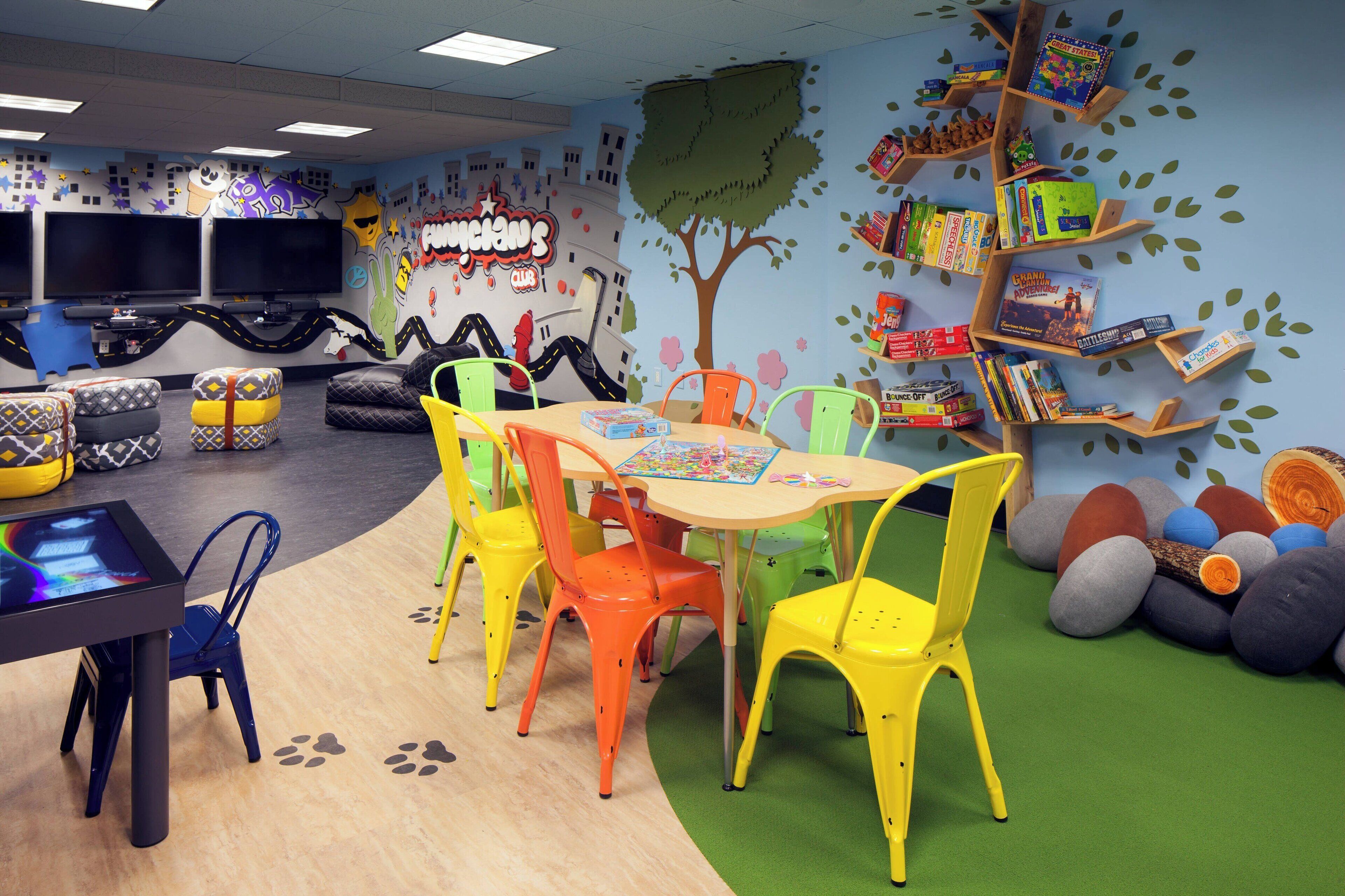 A children's playroom with colorful chairs, a table, and a bookshelf filled with books.