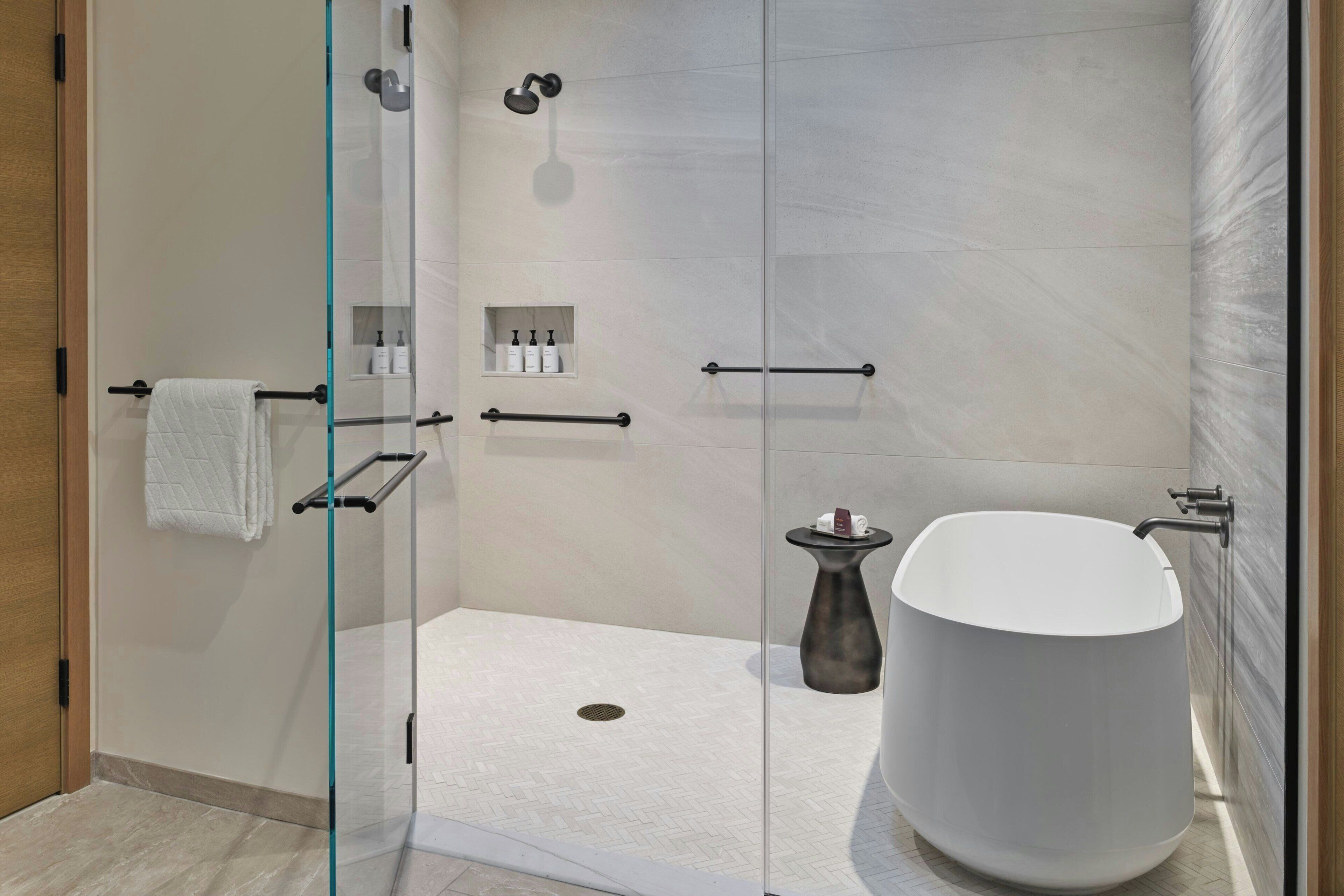 Un baño moderno con ducha envuelta en vidrio, una bañera independiente y un tocador pequeño con artículos de aseo.