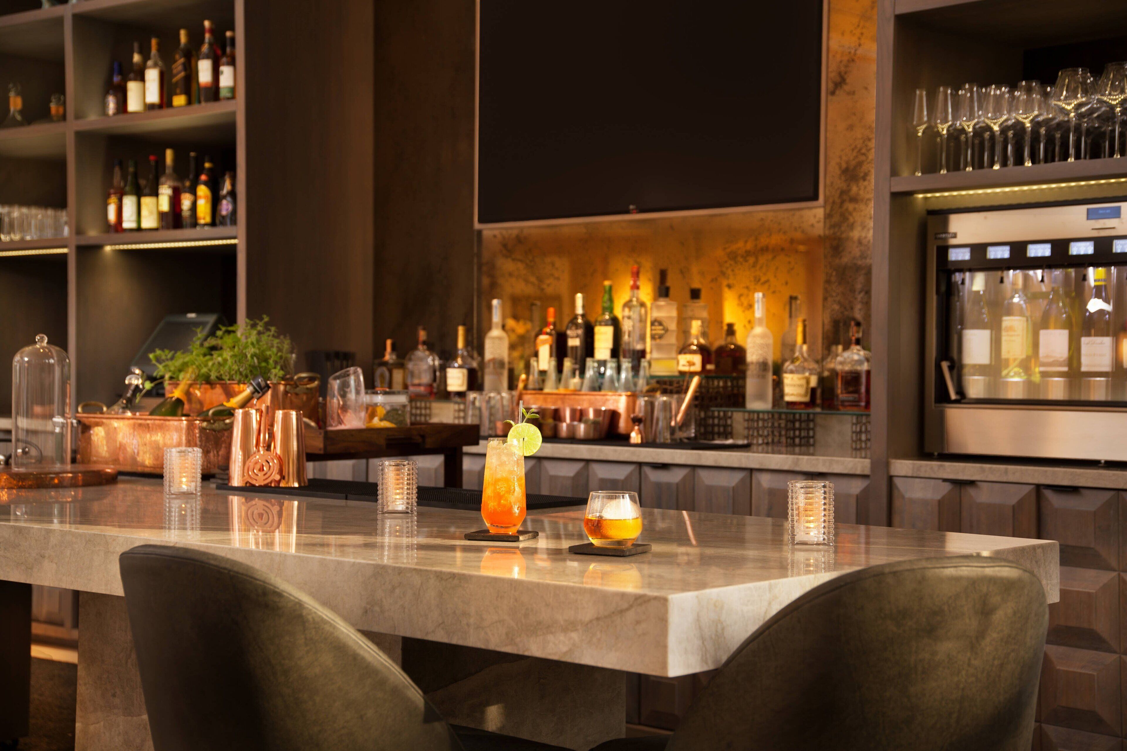 A bar area with a marble countertop, copper bar tools, and a variety of bottles and glasses.