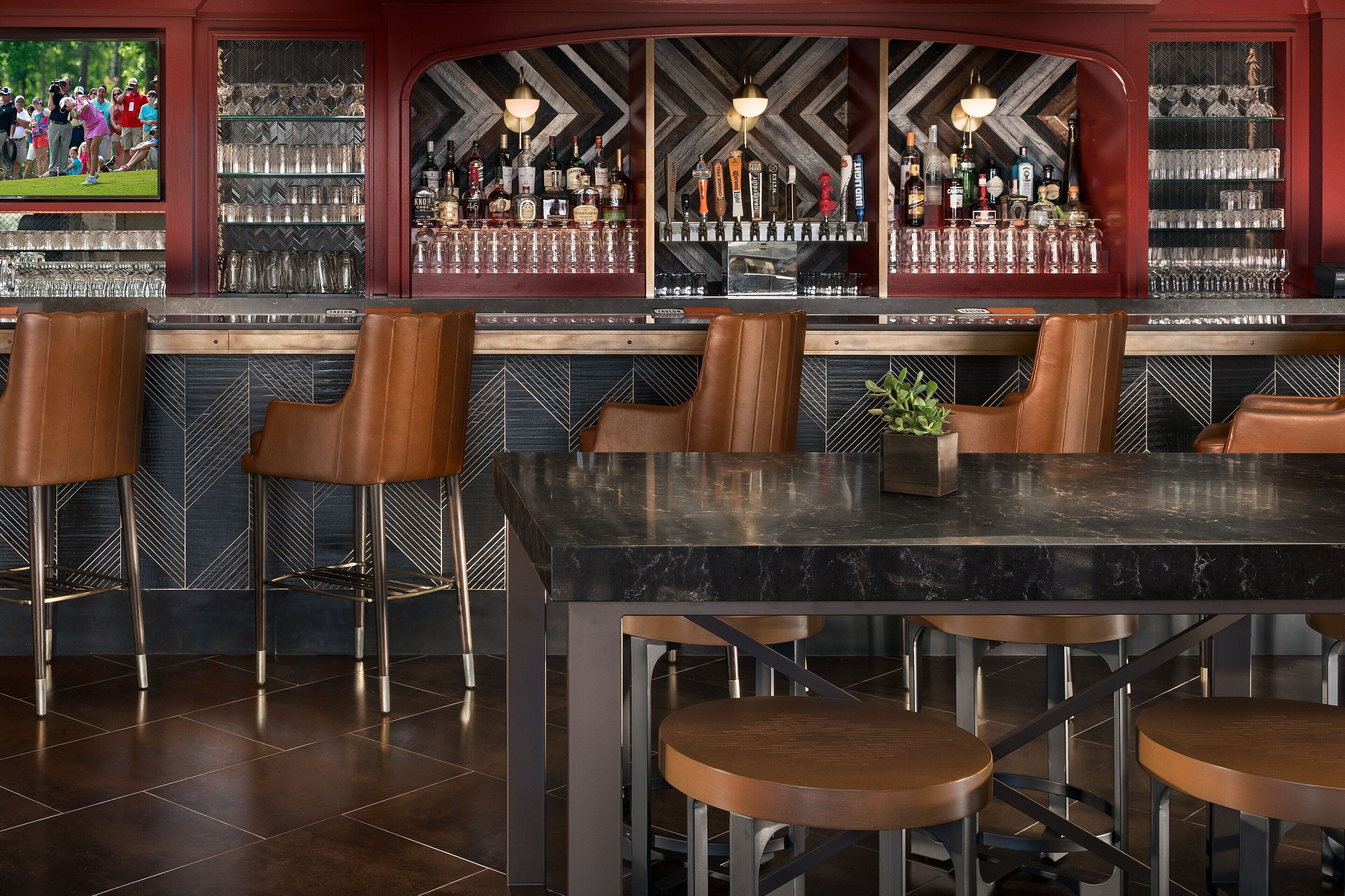A bar area with a marble countertop, leather bar stools, and a variety of bottles and glasses on shelves.
