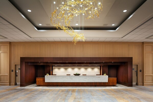 A reception area with a marble counter, wooden panel walls, and a modern chandelier.