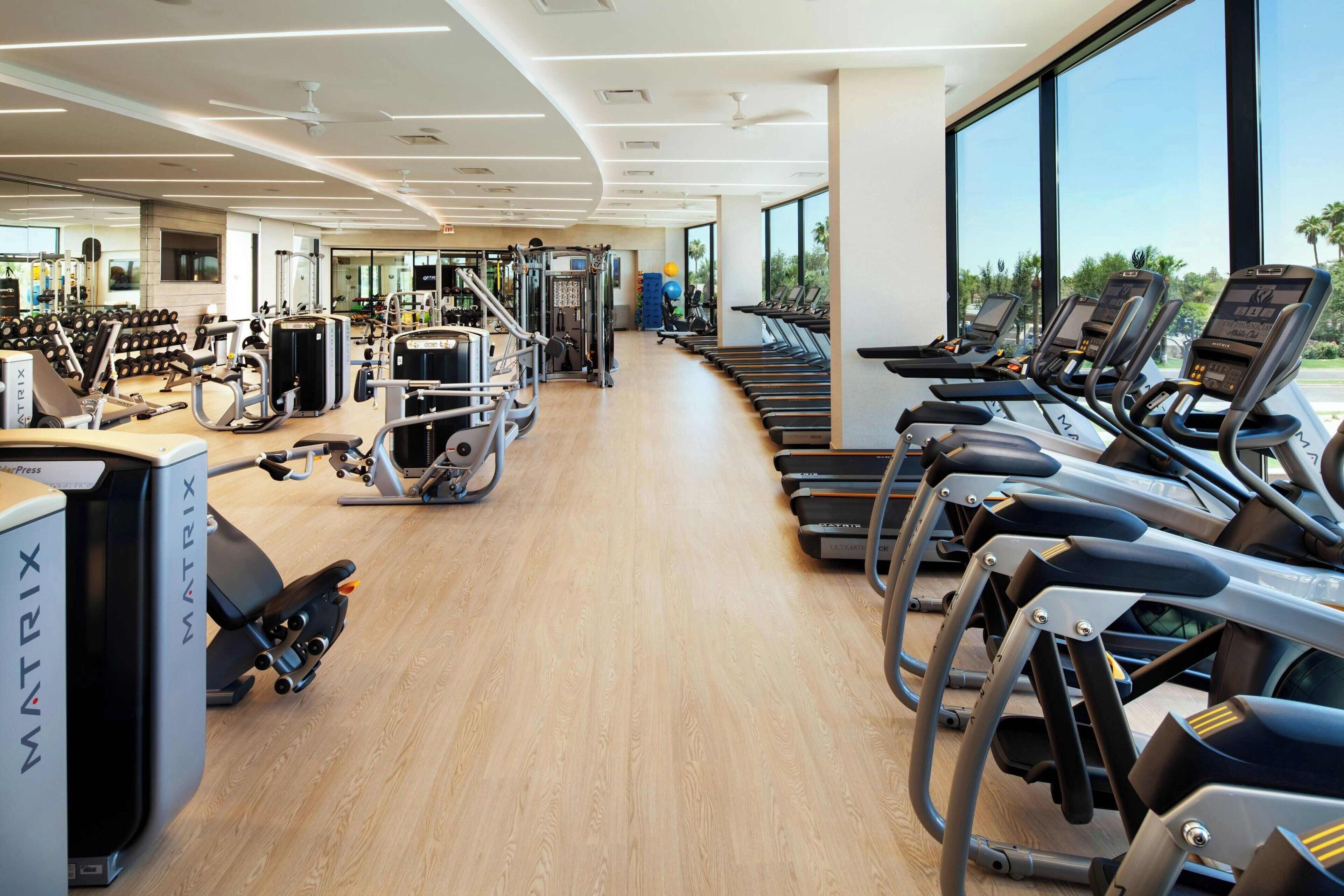 A gym with cardio machines, weightlifting equipment, and a large window offering a view of the outdoors.