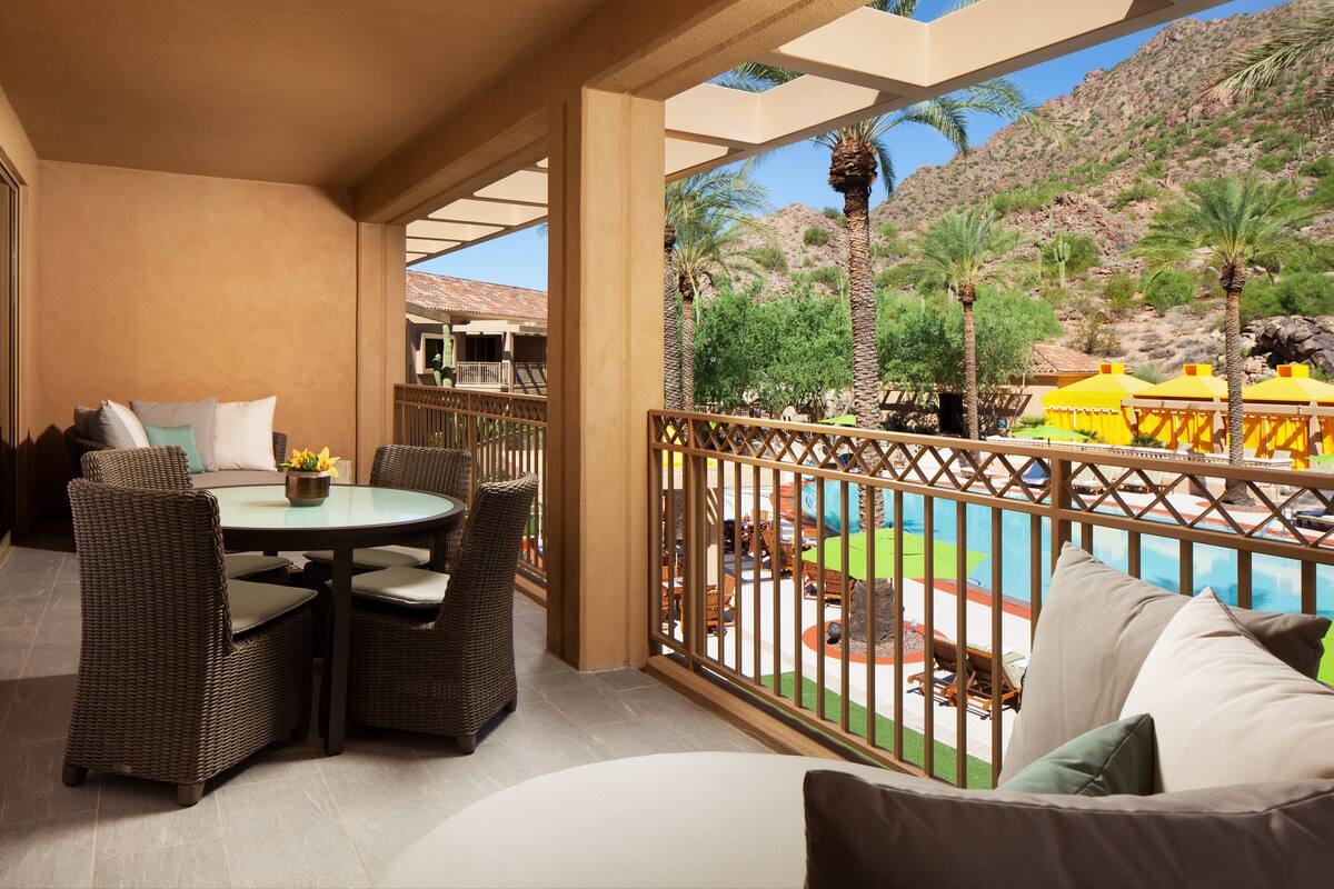 A covered outdoor area with wicker furniture, a pool, and a view of a mountainous landscape.