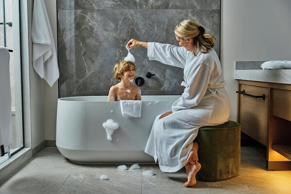 A modern bathroom with a large bathtub, a wooden vanity, and a marble wall.