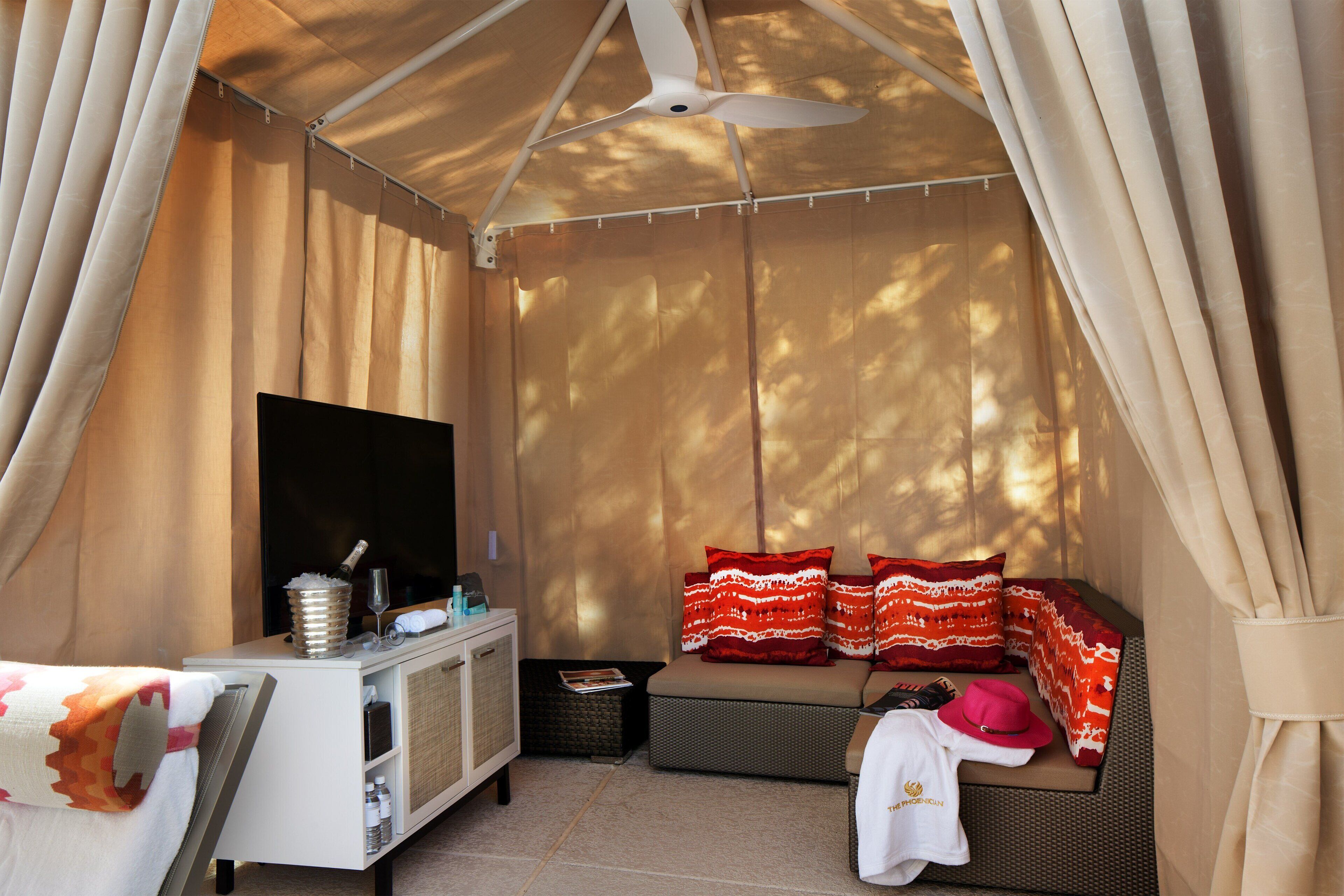 A tented accommodation with a sofa, pillows, a flat-screen TV, and a small table with a bottle and glasses.