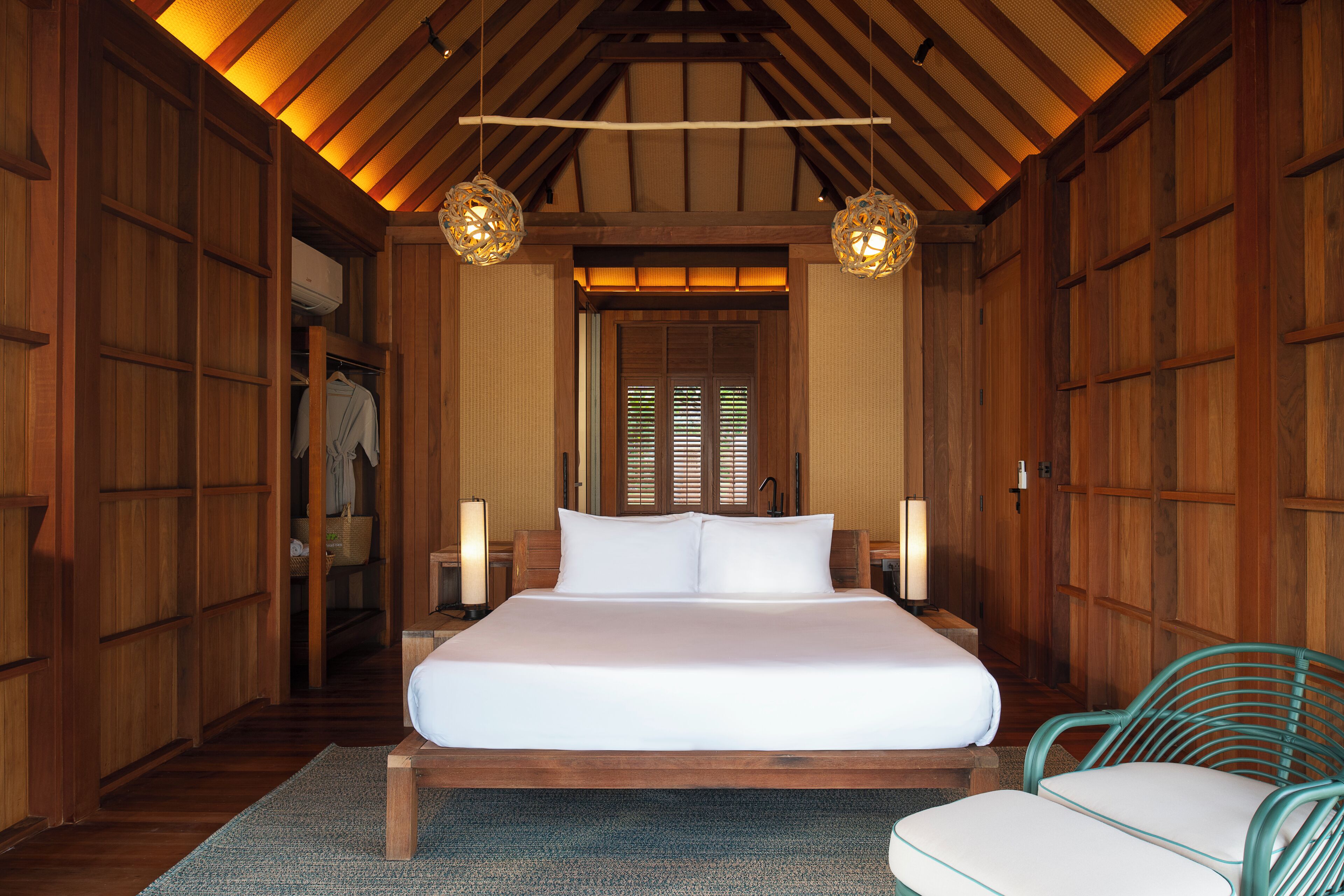 A wooden room with a large bed, two hanging light fixtures, and a chair.