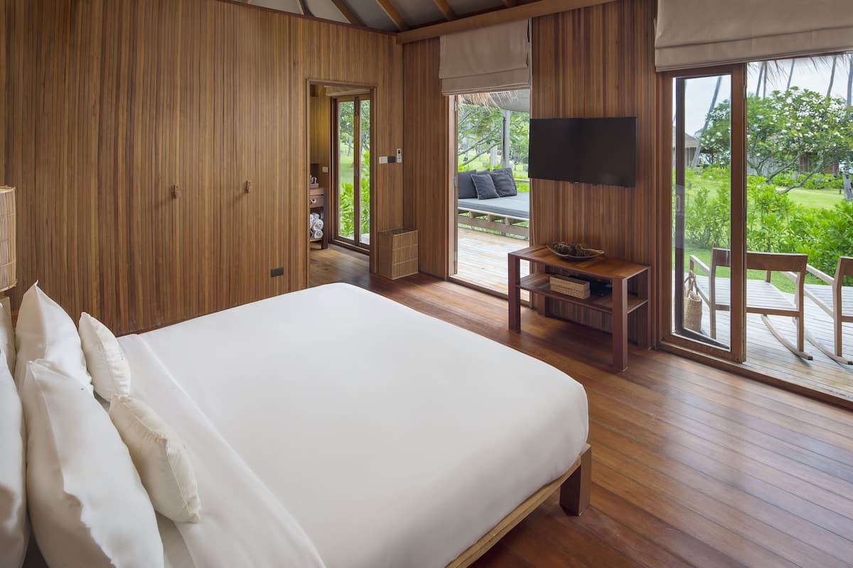 A bedroom with a large bed, wooden walls, a TV, and a view of the outdoors.