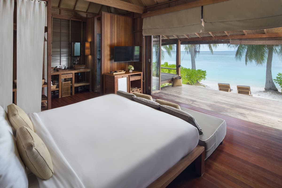 A bedroom with a large bed, wooden desk, TV, and a view of the beach.