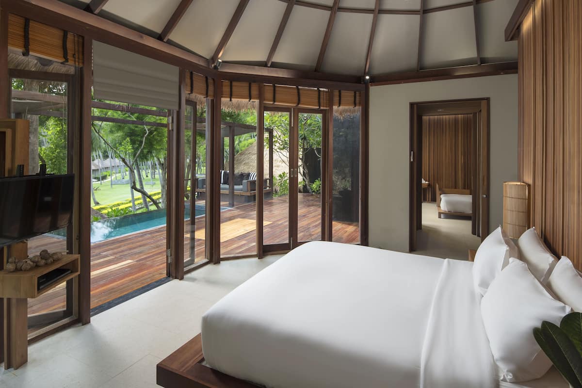 A bedroom with a large bed, a TV, and a view of an outdoor pool area.