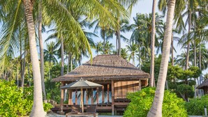 A thatched-roof hut with a bench and umbrella, surrounded by palm trees and greenery. - Haadtien Beach Resort (Koh Tao)