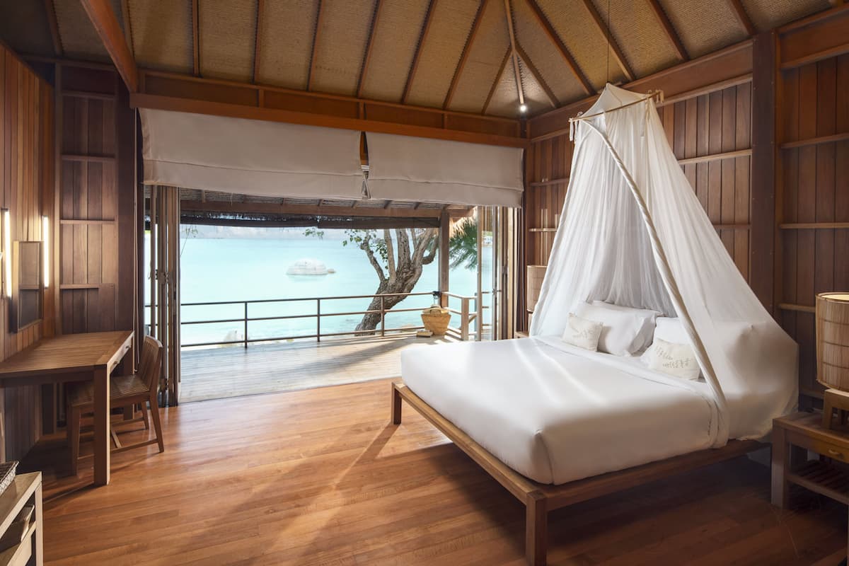 A wooden room with a bed, a table, and a view of the sea.
