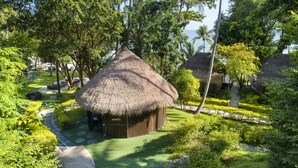 A thatched-roof hut with a paved path leading to it, surrounded by lush greenery and palm trees. - Haadtien Beach Resort (Koh Tao)
