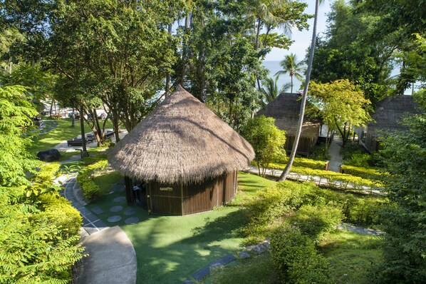 A thatched-roof hut with a paved path leading to it, surrounded by lush greenery and palm trees. - Haadtien Beach Resort (Koh Tao)