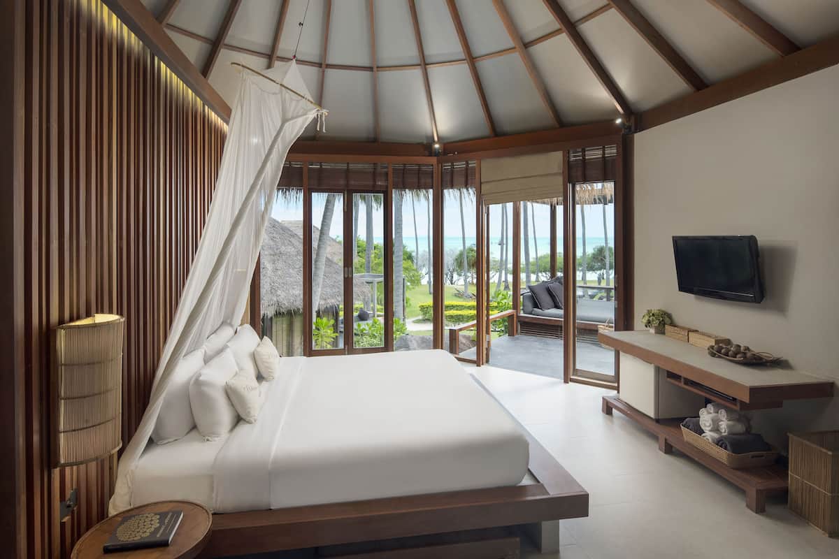 A bedroom with a bed, bedside table, TV, and a view of the outdoors.