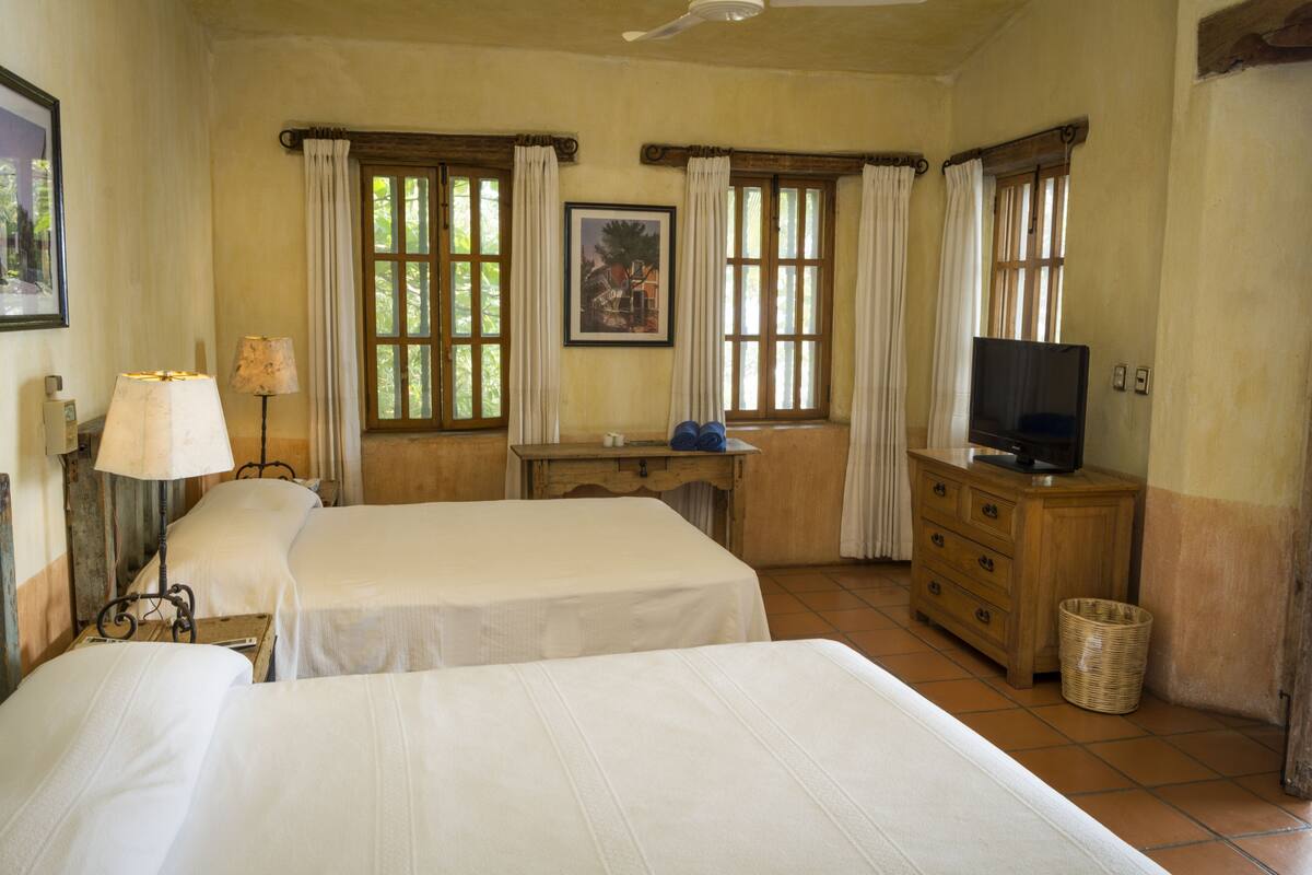 A room with two beds, a desk, a television, and a window with curtains.