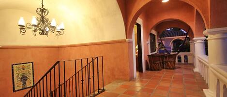 A spacious hallway with a tiled floor, a staircase with a black railing, and a chandelier with multiple light fixtures.