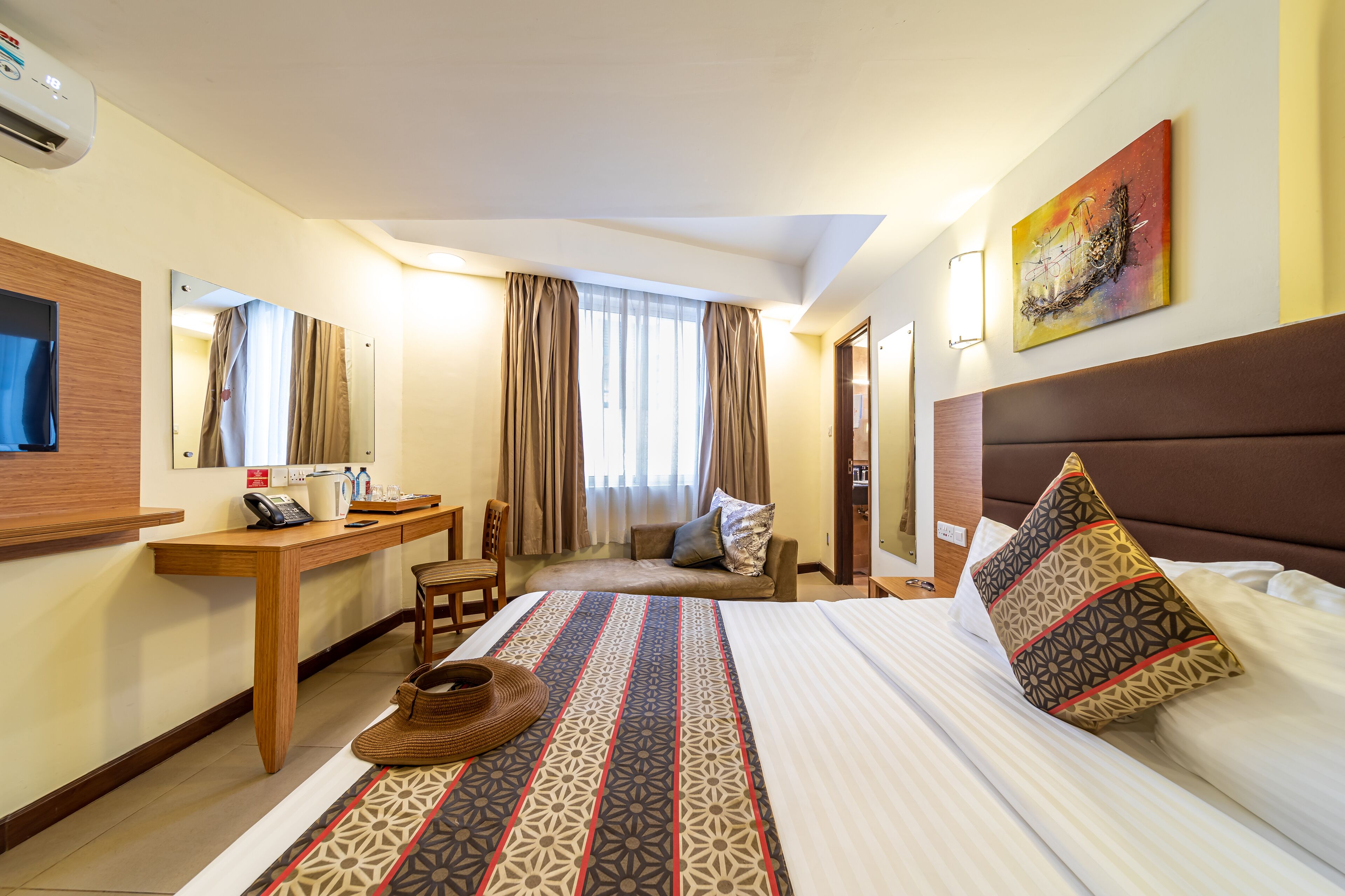 A hotel room with a bed, a desk, a chair, a telephone, and a window with curtains.