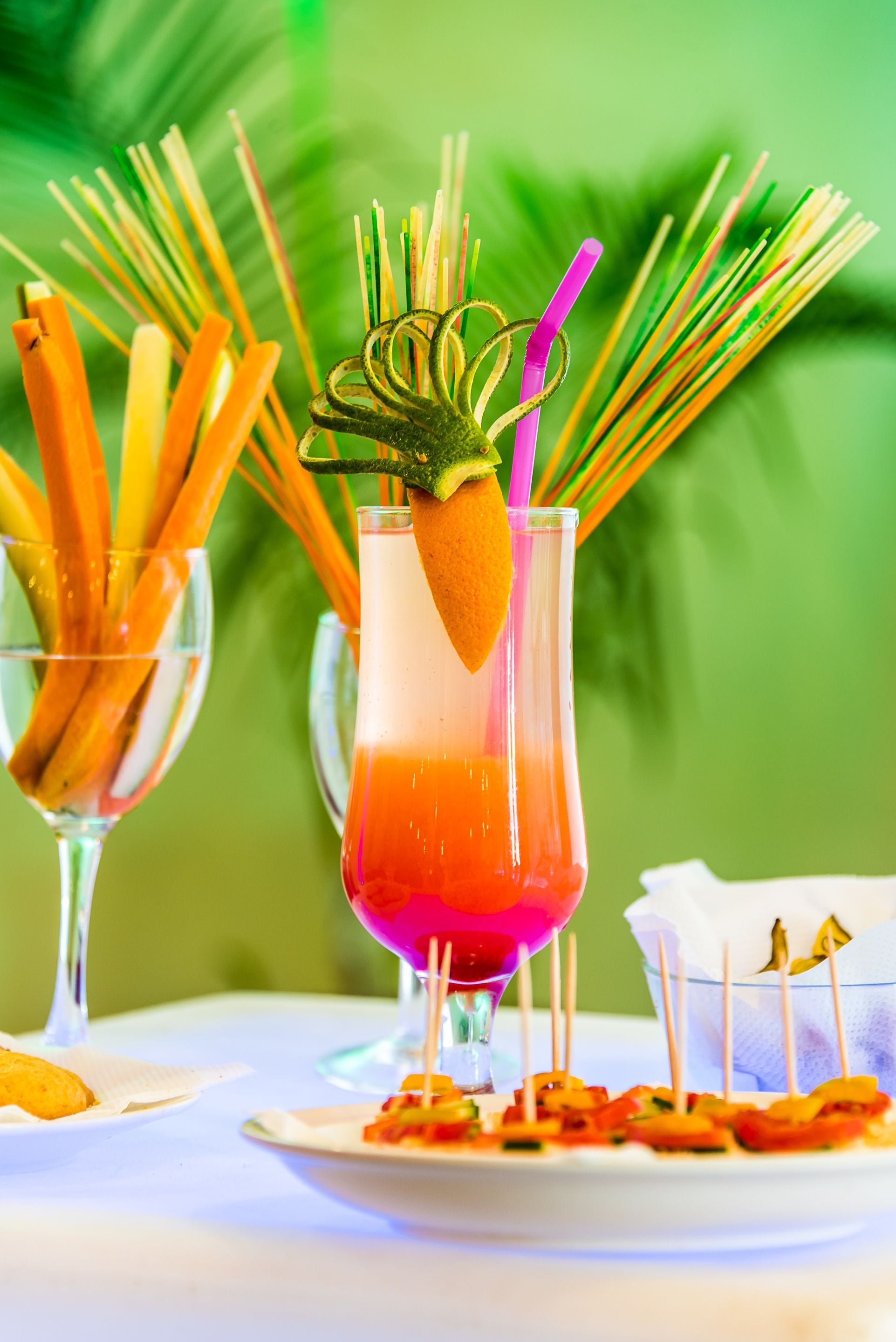 Un cóctel con una decoración de fresa y una pajita de colores, rodeado de brochetas de frutas y verduras.