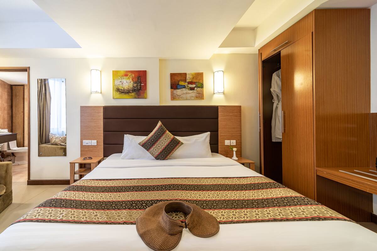 A hotel room with a large bed, a wooden wardrobe, two wall-mounted lamps, and two paintings.