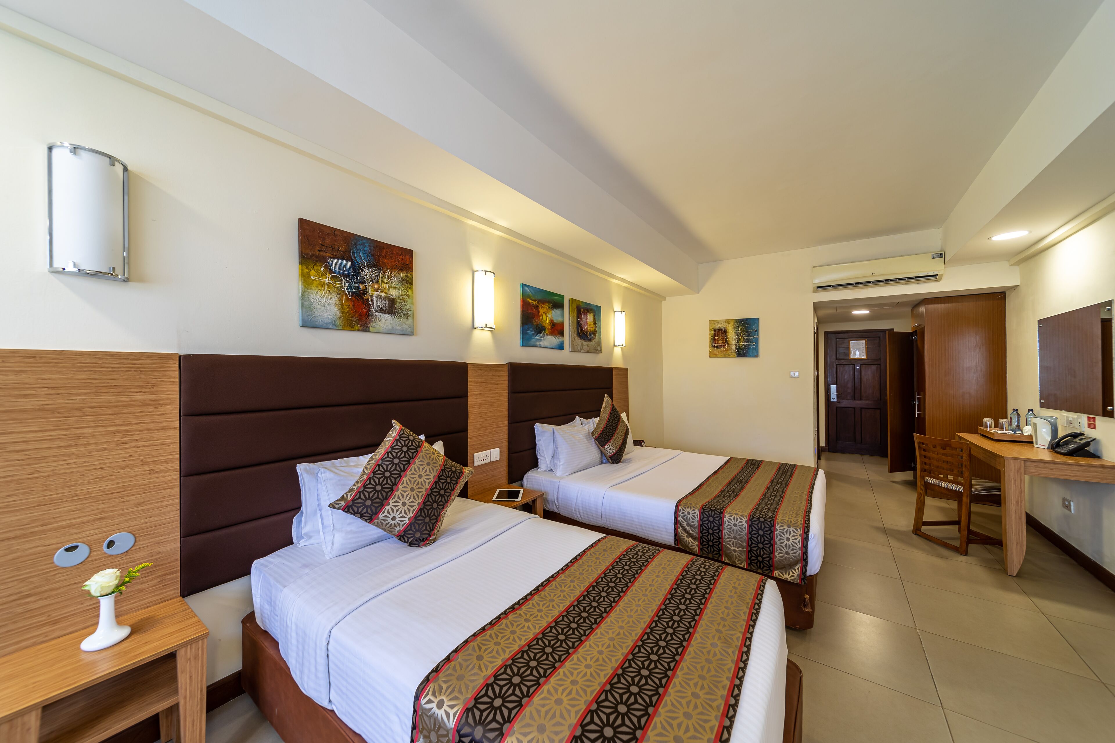 A hotel room with two beds, a desk, a chair, and artwork on the walls.