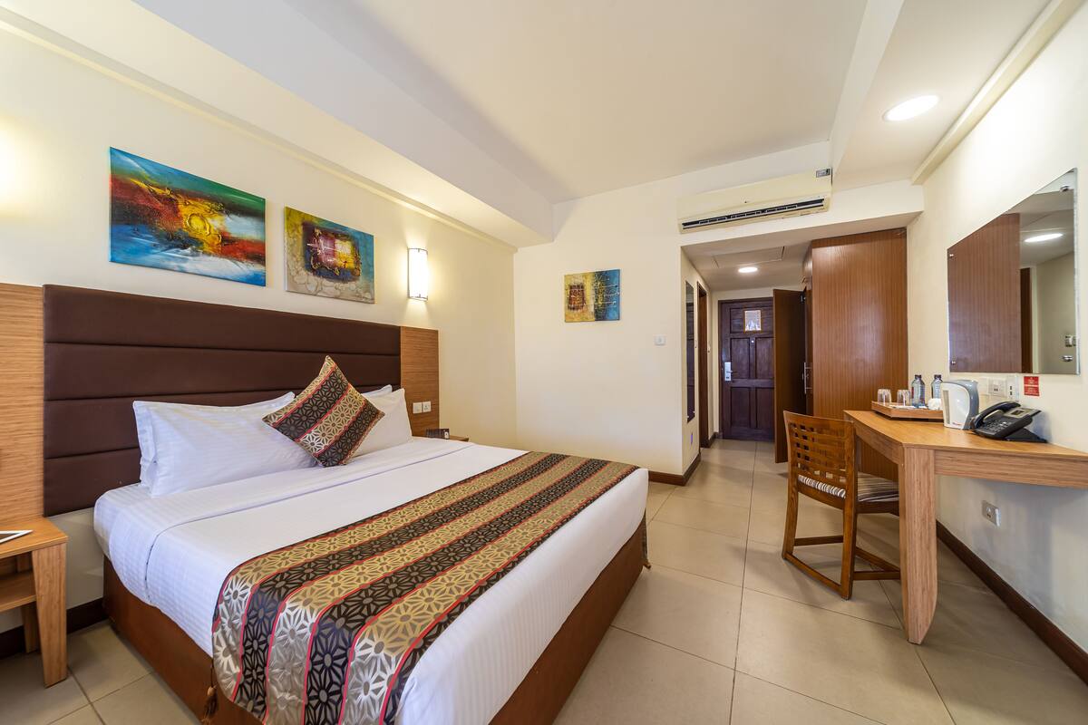 A hotel room with a large bed, a wooden desk, a chair, and artwork on the walls.