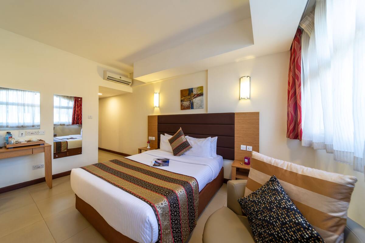 A hotel room with a large bed, bedside tables, a desk, and a window with curtains.