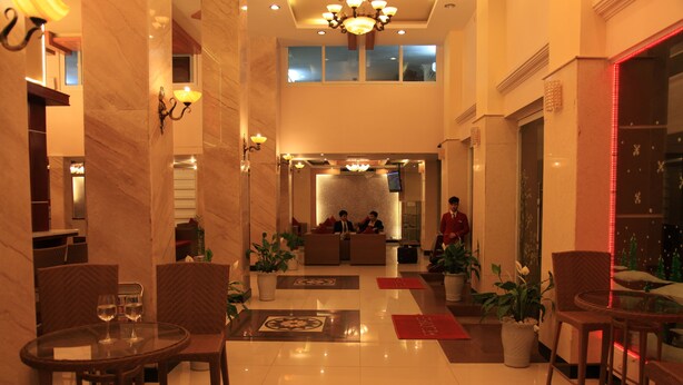 A hotel lobby with a reception desk, seating area, and a glass table with two wine glasses. - Princes Catba Hotel (Hai Phong)