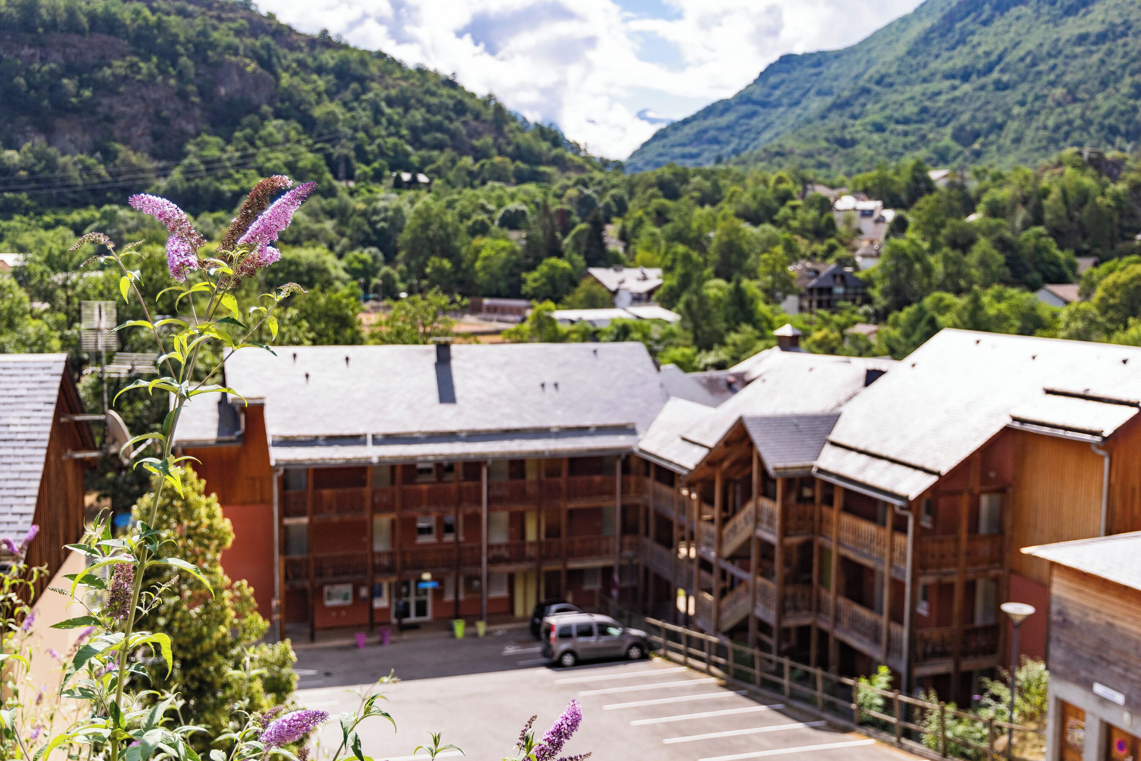 A building with a parking lot, surrounded by greenery and mountains.