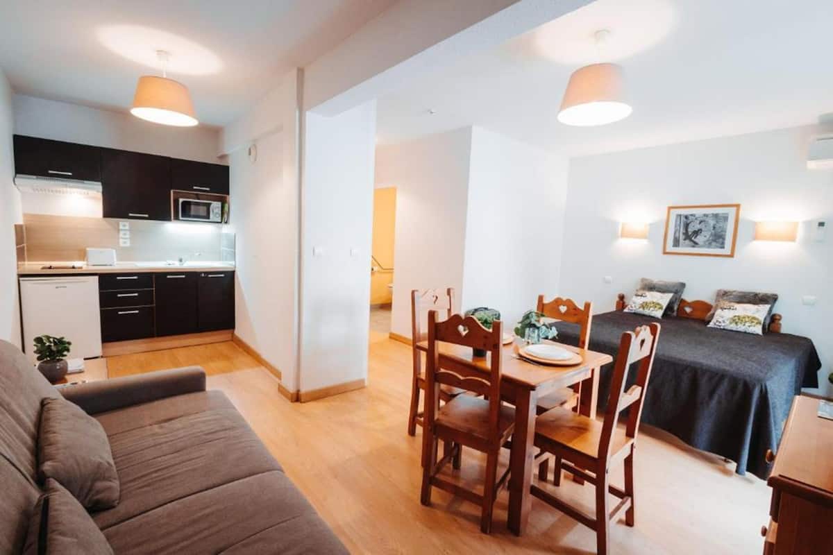 A compact living space with a kitchenette, a dining area, and a bed with a dark bedspread.