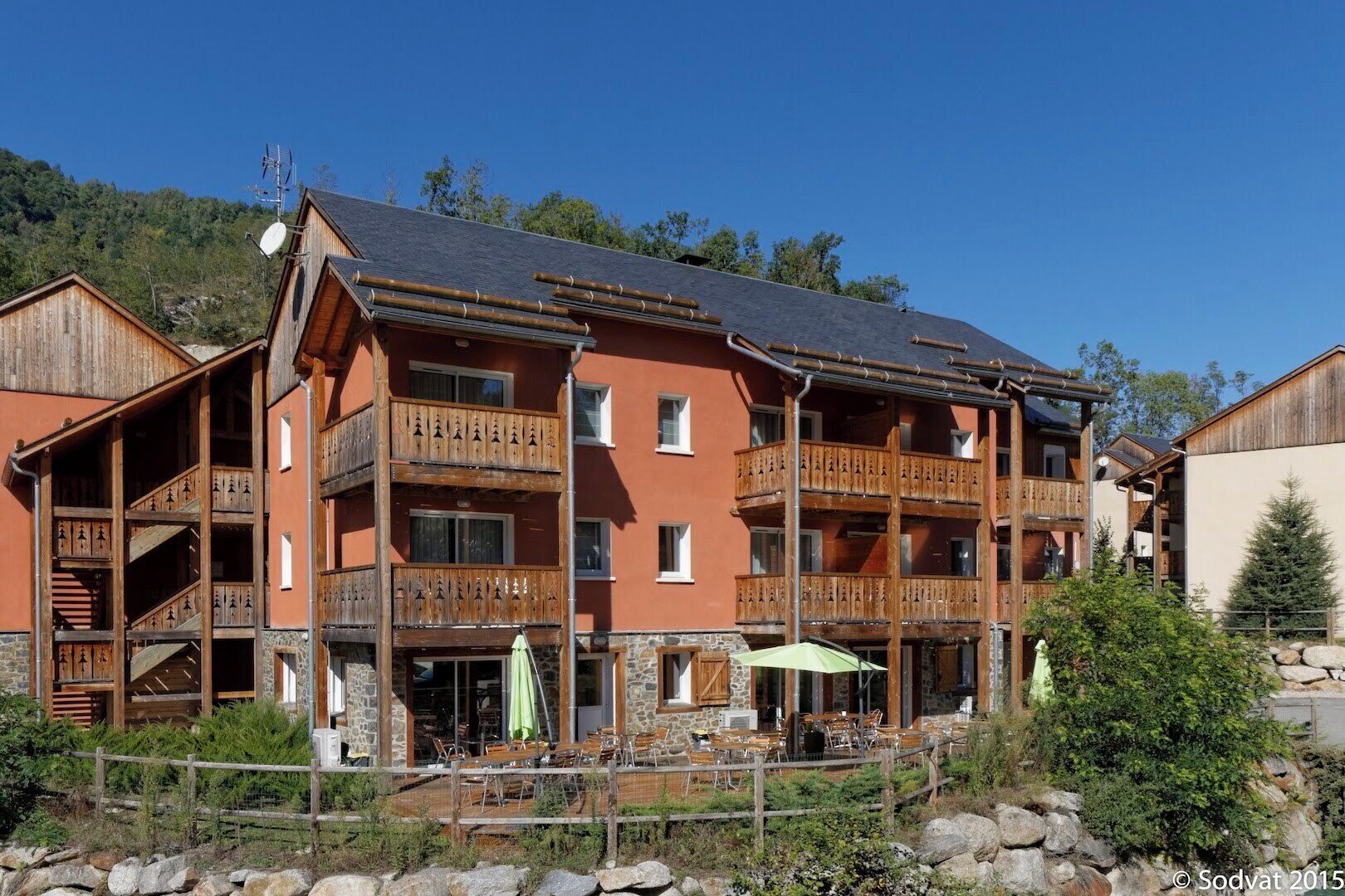 Ein mehrstöckiges Holzgebäude mit Balkonen, Außenbestuhlung und einer Steinfassade.