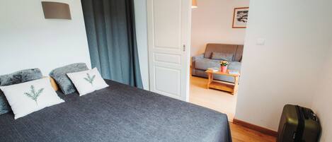 Un dormitorio con una cama grande, una maleta y vistas a una sala de estar con un sofá y una mesa.