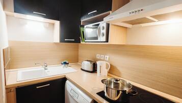 A compact kitchen with a dishwasher, a microwave, a toaster, and a kettle.
